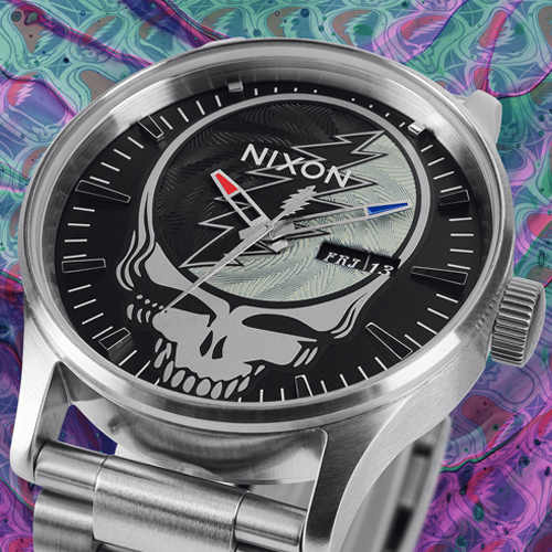 A Nixon watch with a black face featuring the Grateful Dead's Steal Your Face skull logo and a lightning bolt design, set against a colorful, psychedelic background.