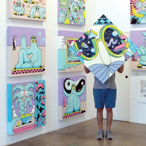 A man holds up a Steven Harrington painting while standing in a gallery.