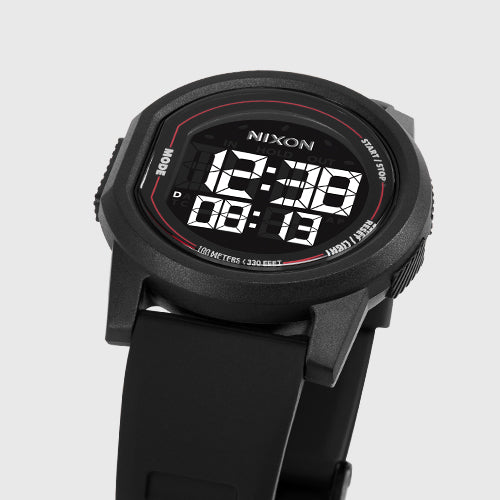 A close-up shot of a black Nixon digital watch with a black strap, displaying the time 12:38.