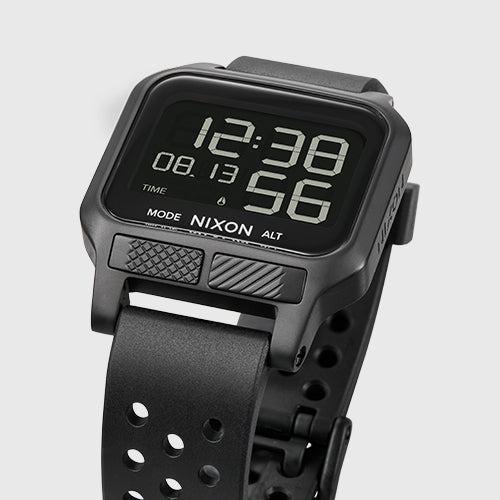 A close-up shot of a black Nixon digital watch with a perforated strap and a display showing 12:38 and 56.