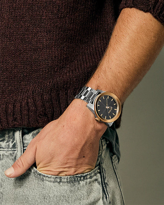 Nixon watch with bronze bezel and silver band on a man.