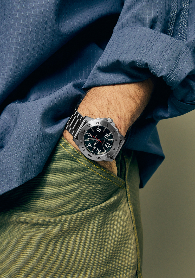 Man wearing a silver Nixon Smyth 44 analog watch with his hand in his pocket